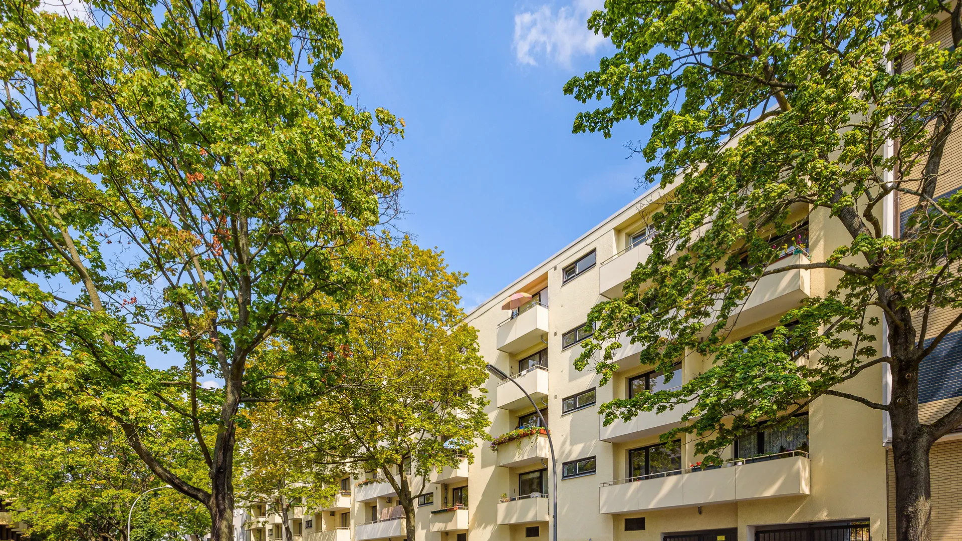 Gelbe Wohnanlage mit Balkonen hinter Straßenbäumen in Berlin-Wilmersdorf